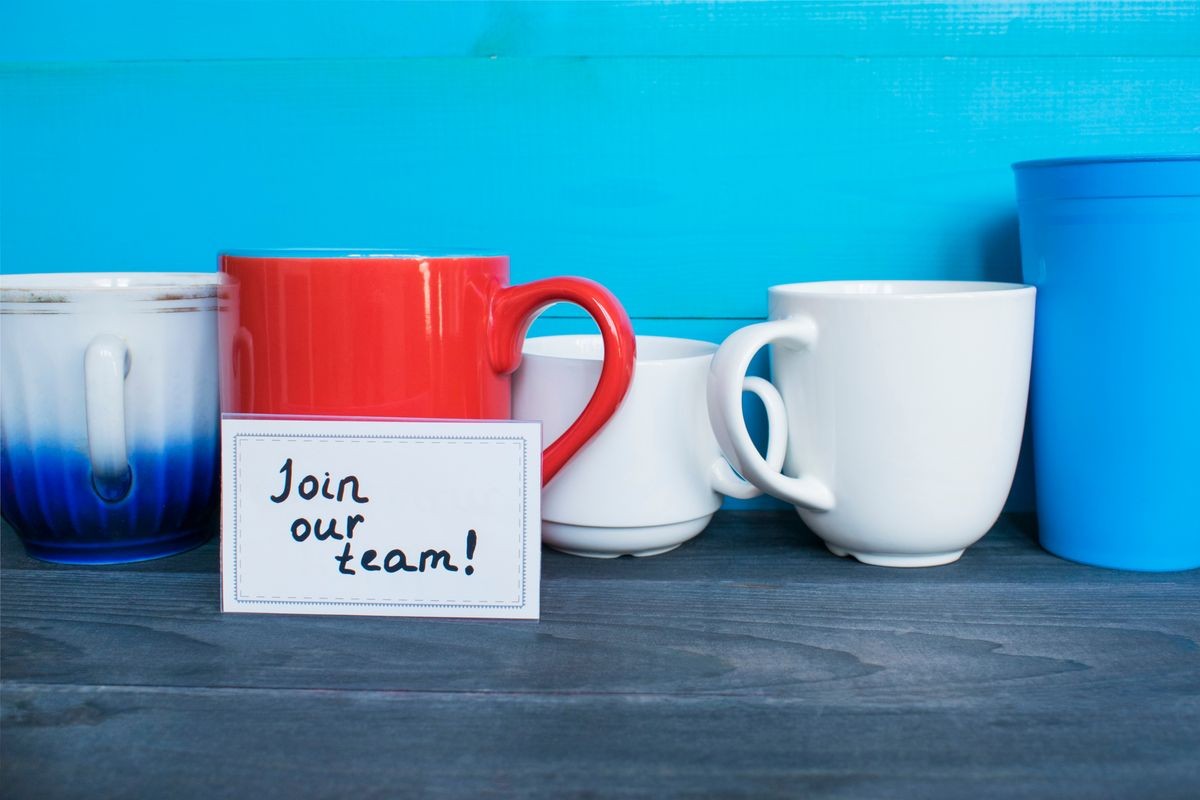 Red mug with words Join our team on the wooden table. 