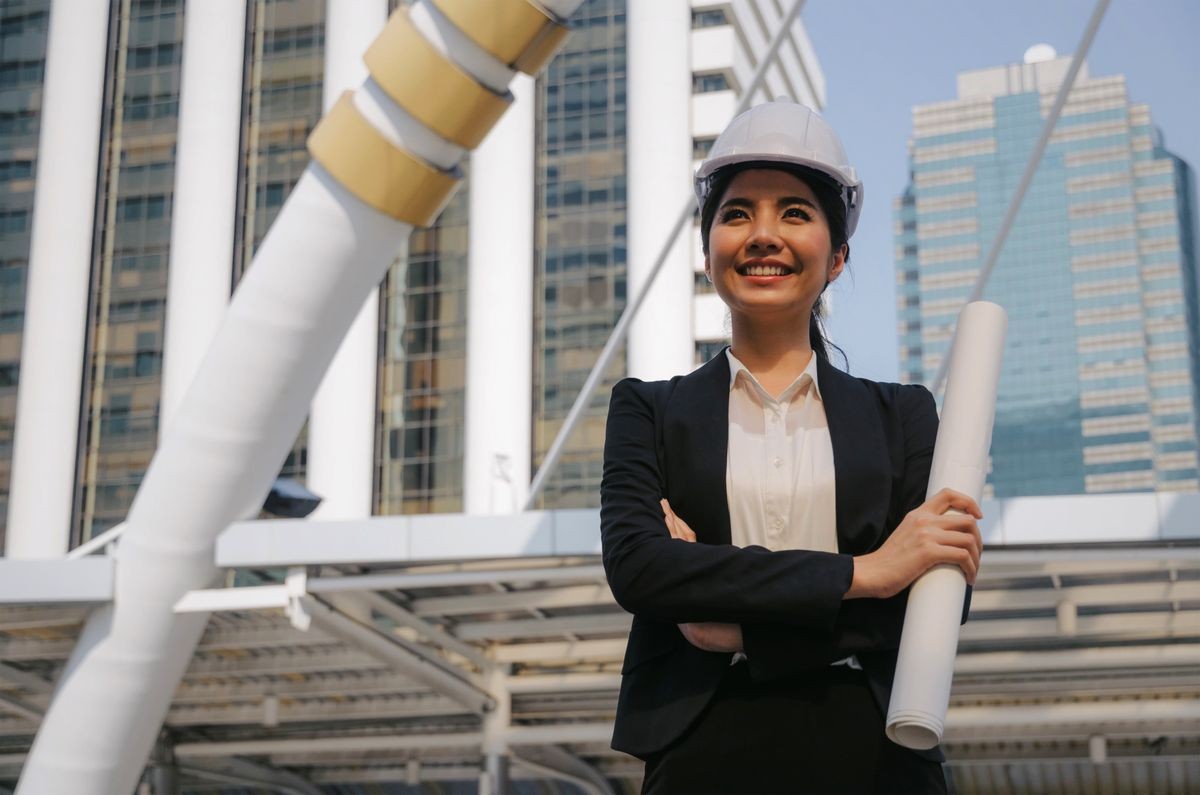 young asian business, engineer or technician woman in suit with white safety helmet looking to future and arms crossed in big city building background, business, industry and construction concept